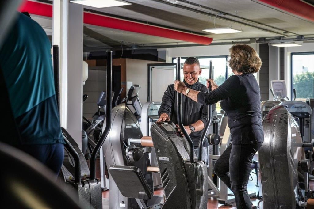 Man en vrouw in een sportschool, lachend en interactief bij crosstrainers. Fitnessomgeving.