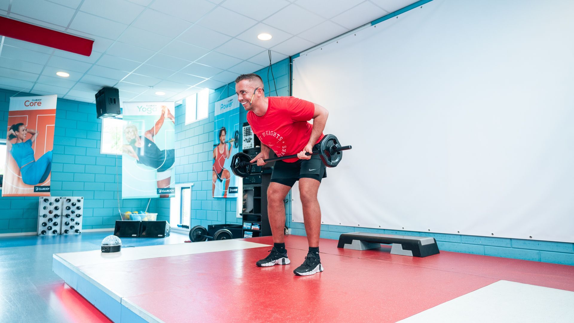Persoon staat met zijn voeten dicht bij een halter op de vloer van een sportzaal.
