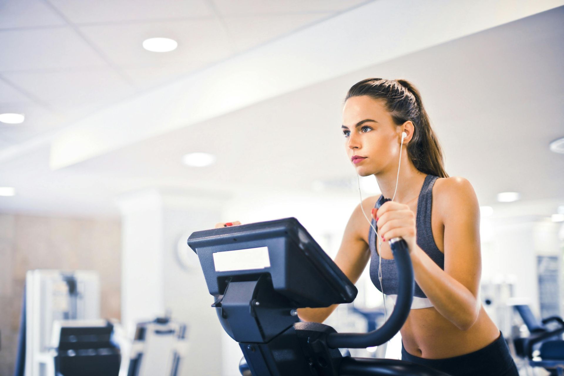 Een vrouw traint op een crosstrainer in de sportschool en luistert naar muziek.