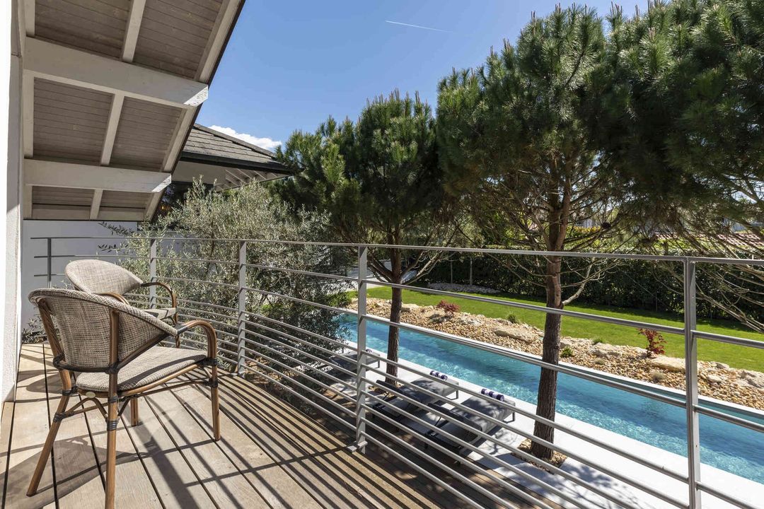 Balcony with wicker chair overlooking a swimming pool and trees in bright sunlight