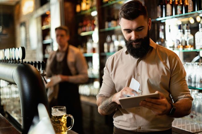 Bartender writing on a notepad behind a bar, with glasses and bottles in the background.