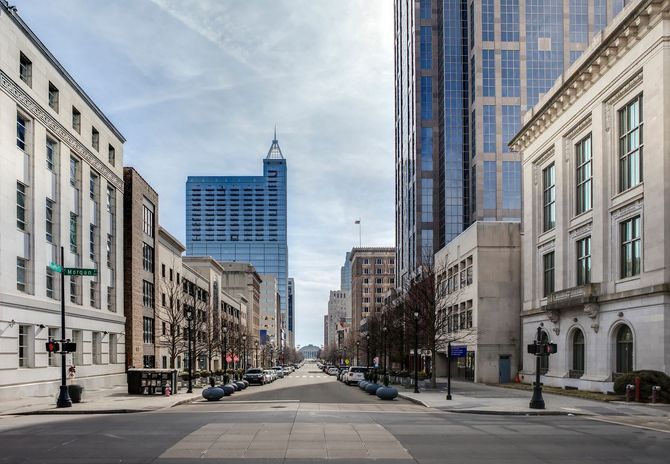 Empty city street lined with buildings, leading toward a blue glass tower under a bright sky