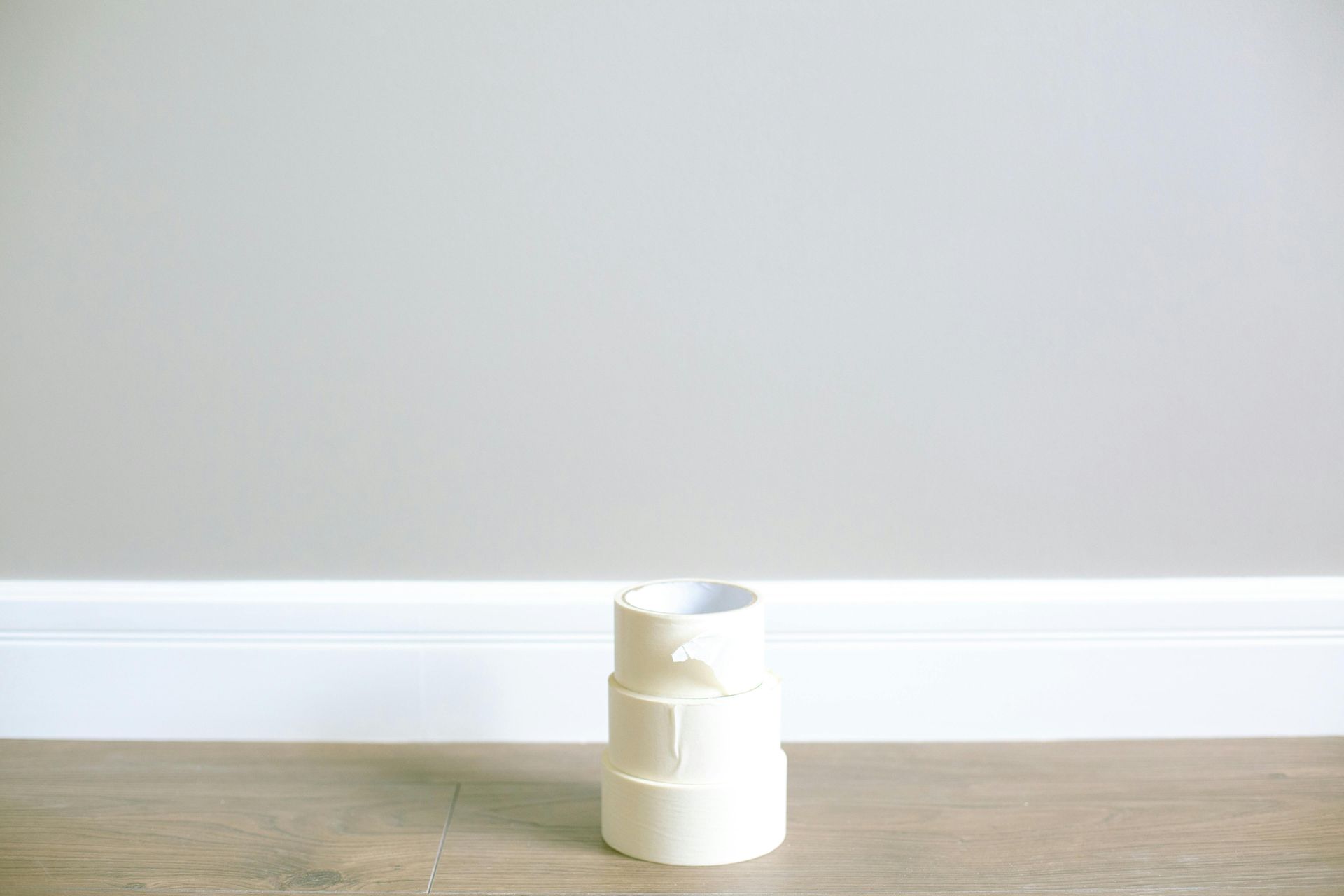 Three rolls of tape are stacked on top of each other on a wooden floor.