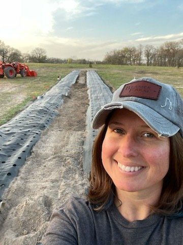 A woman is taking a selfie in a field with a tractor in the background.
