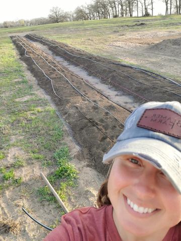 A woman wearing a hat is taking a selfie in a field.