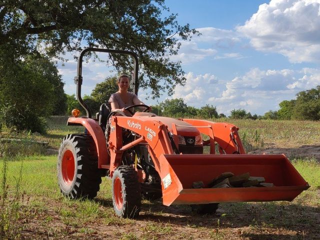 A woman is driving an orange tractor in a field.