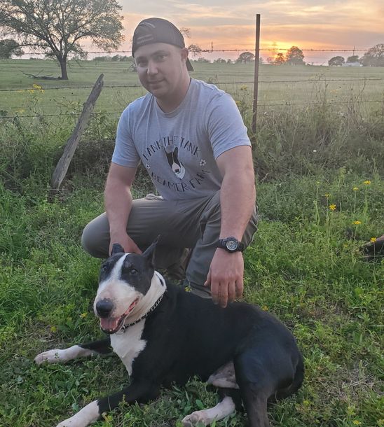 A man is kneeling down next to a black and white dog in a field.