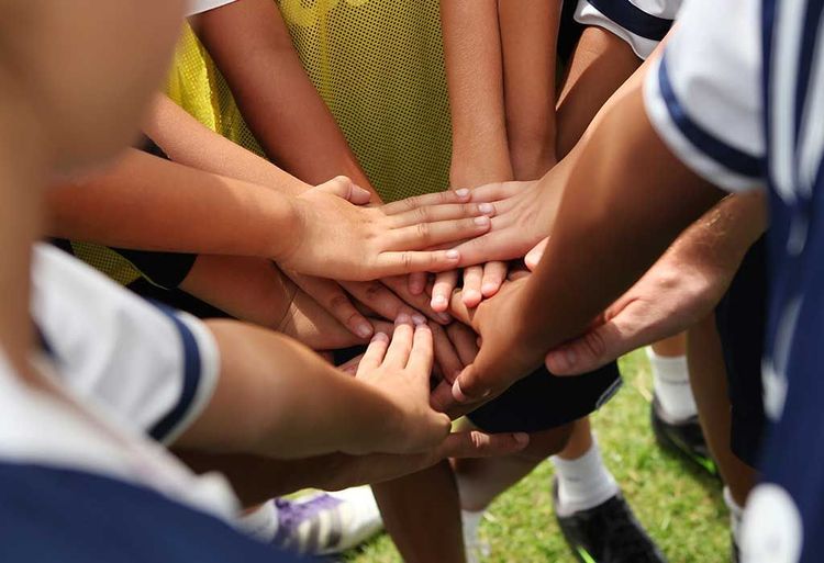 Hands stacked together in a sports team huddle on a grassy field.
