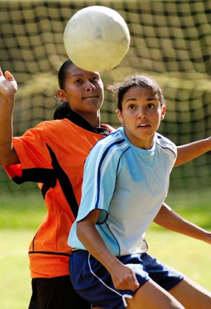 Two youths in orange and light blue jerseys contest a soccer ball outdoors