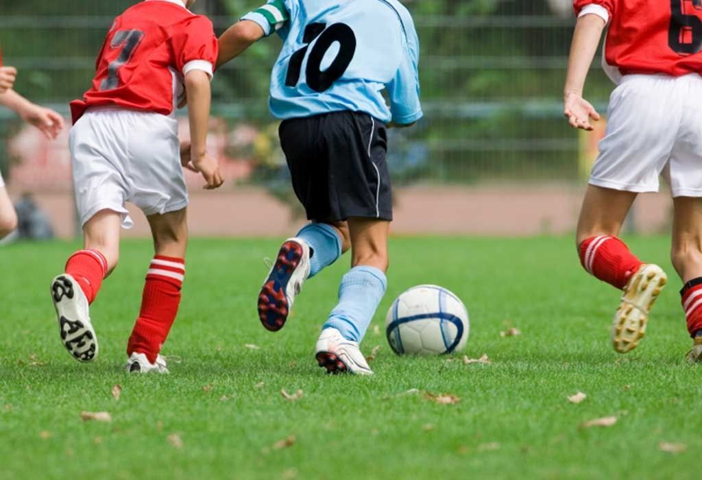 Youth soccer players running after a ball on a grassy field, with red and blue uniforms.