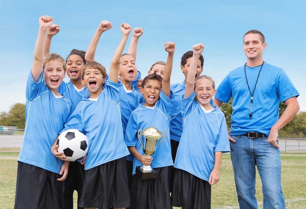 Youth soccer team in blue jerseys celebrating with a trophy and soccer ball on a field