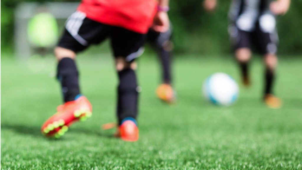 Soccer players’ legs in motion on a green field, with a ball near the foreground.