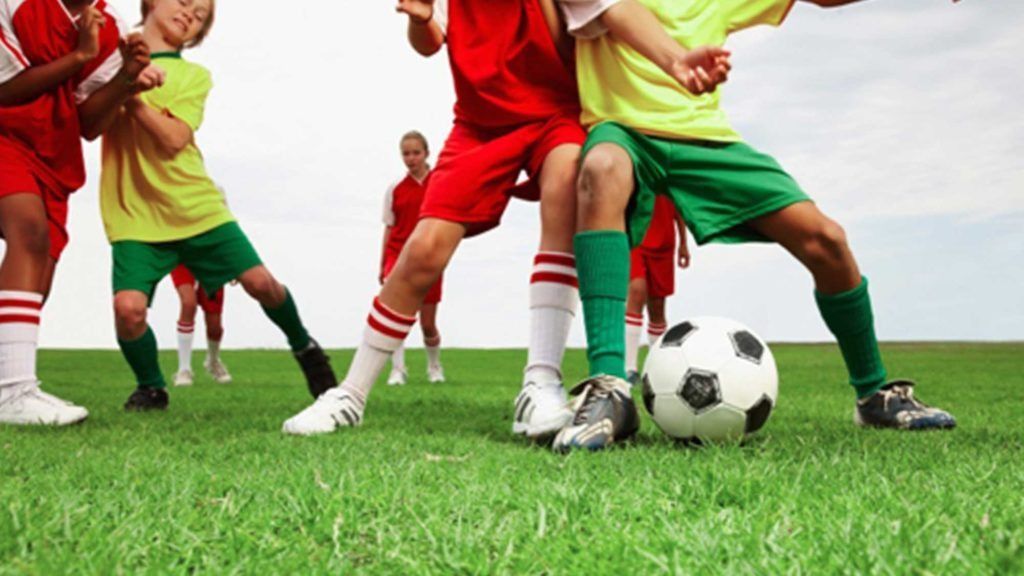 Youth soccer players in red and green uniforms competing for the ball on a grassy field