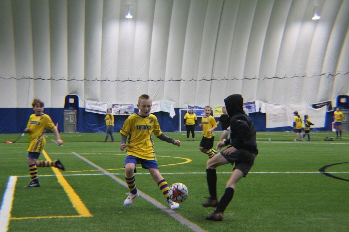 Indoor youth soccer game with players in yellow and black contesting the ball on turf