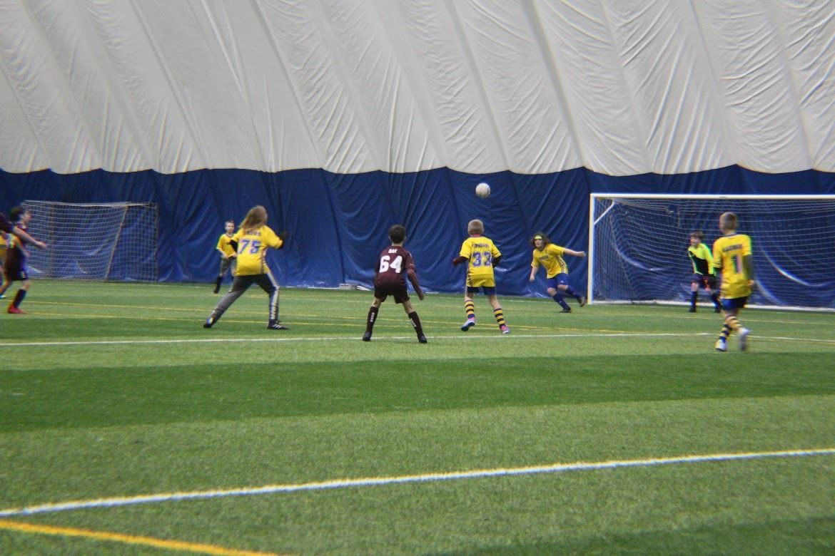 Soccer players in yellow and black contesting a play near the goal on an indoor field