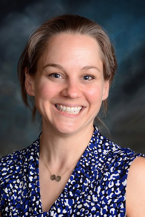 Smiling woman in a blue patterned blouse against a dark studio backdrop