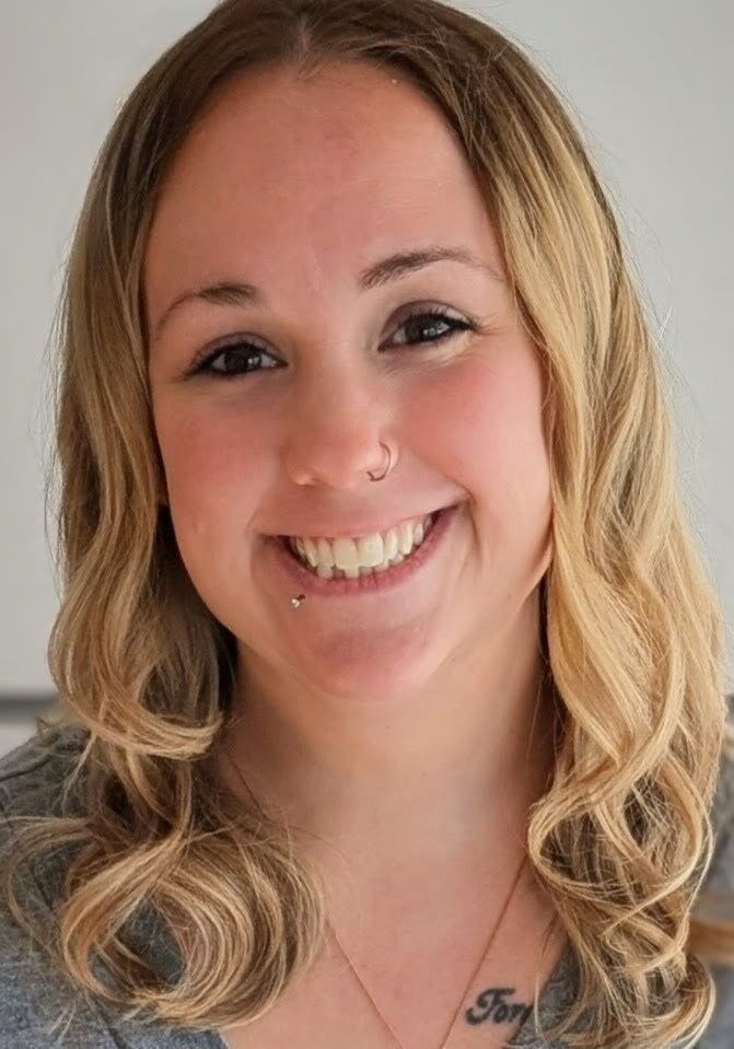 Smiling person with shoulder-length blonde hair against a light background