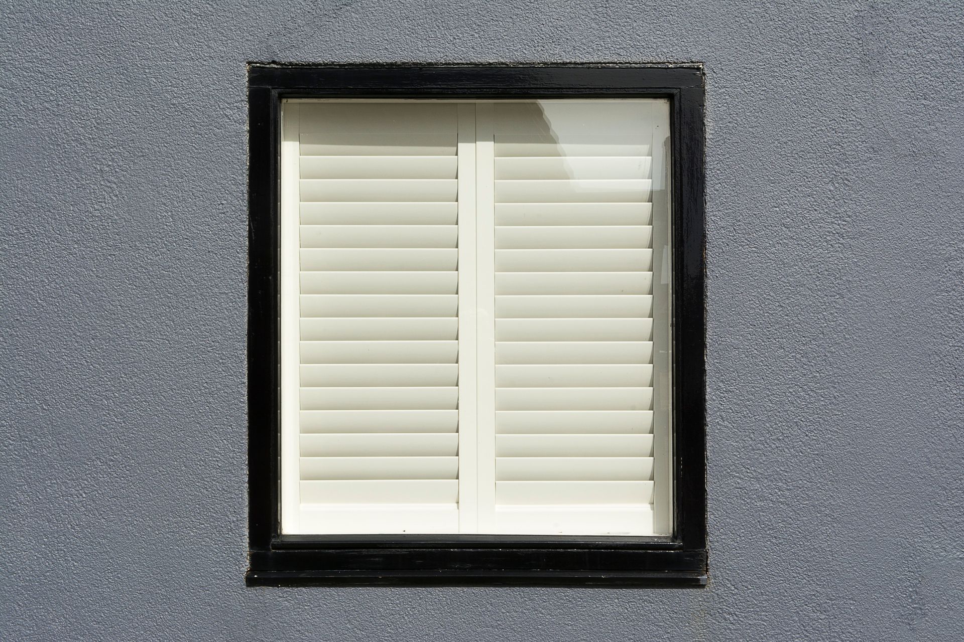 White window shutters in a black frame set in a gray wall.