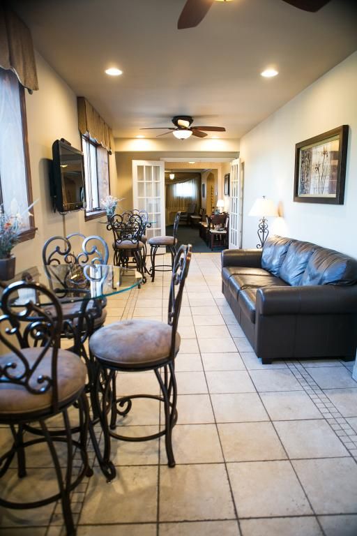 Long, narrow room with bar-style seating, glass-top table, brown leather sofa, and French doors leading to another room.