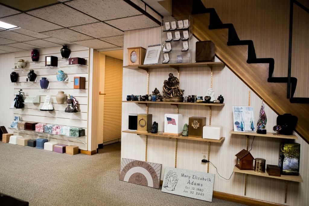 Display of urns and keepsakes in a room, with shelves, stairs, and a door visible.
