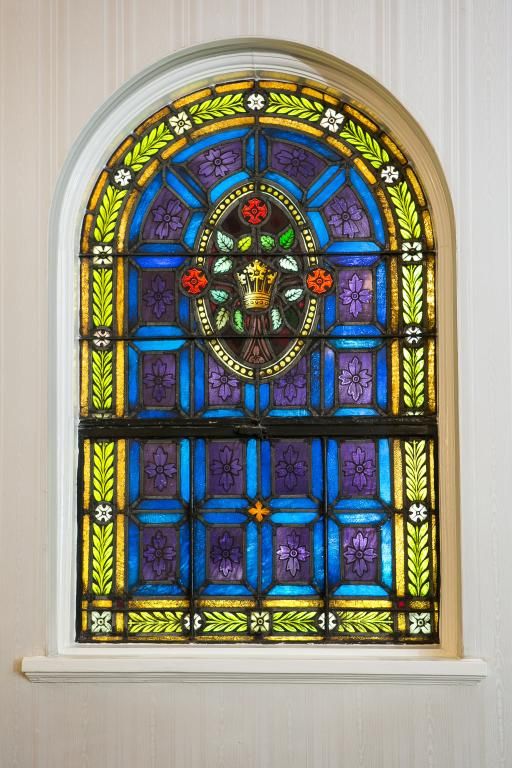 Stained glass window with arched top; blue, purple, green, and gold colors; central oval design with crown.