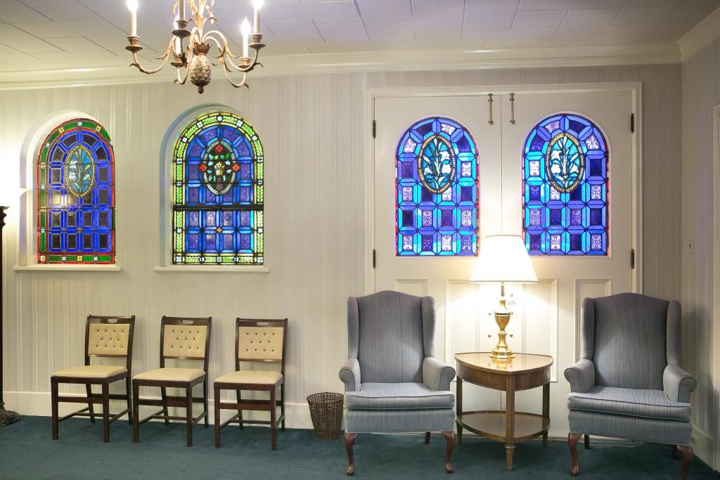 Interior of a room with stained glass windows, chairs, and a chandelier; possibly a chapel.