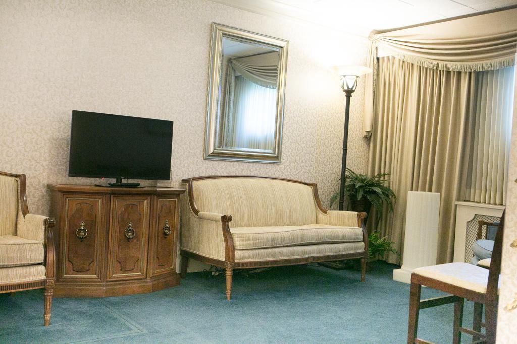 Living room with a sofa, chairs, TV, mirror, and curtains. Light blue carpet.