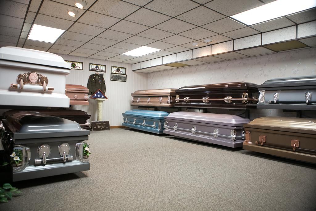 A funeral home showroom displaying various caskets of different colors and styles.