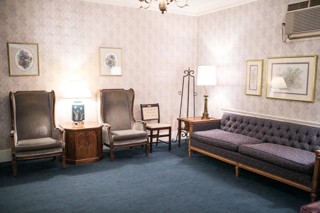 Funeral home waiting area with patterned wallpaper, blue carpet, and vintage furniture.