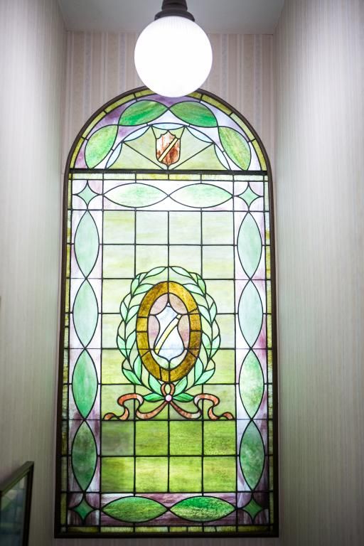 Stained glass window with green, gold, and white hues. Oval emblem with banner is surrounded by a laurel wreath.