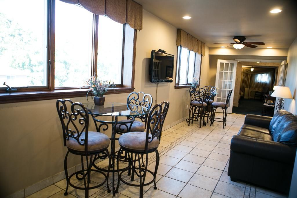 Lounge area with ornate tables and stools, a black leather couch, and windows.