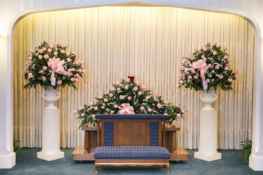 Altar with floral arrangements, pink roses, and draped backdrop. White columns flank the central wooden bench.