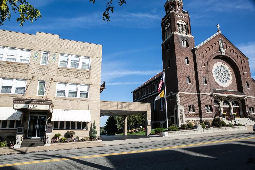 Brick church and light beige building connected by a walkway under a blue sky.