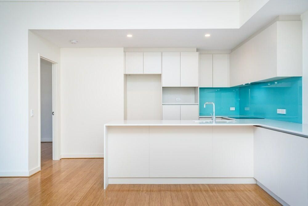 Bright modern kitchen with white cabinets, turquoise backsplash, and wood floors — Mackay Cabinetmaking Service In Glenella, QLD
