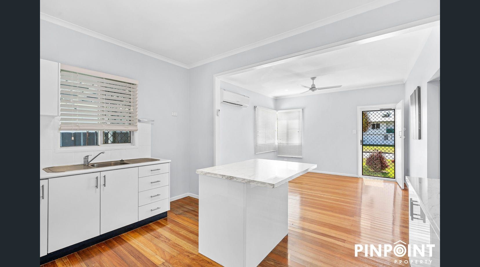 Bright empty kitchen with white cabinets, island, and hardwood floors — Mackay Cabinetmaking Service In Glenella, QLD