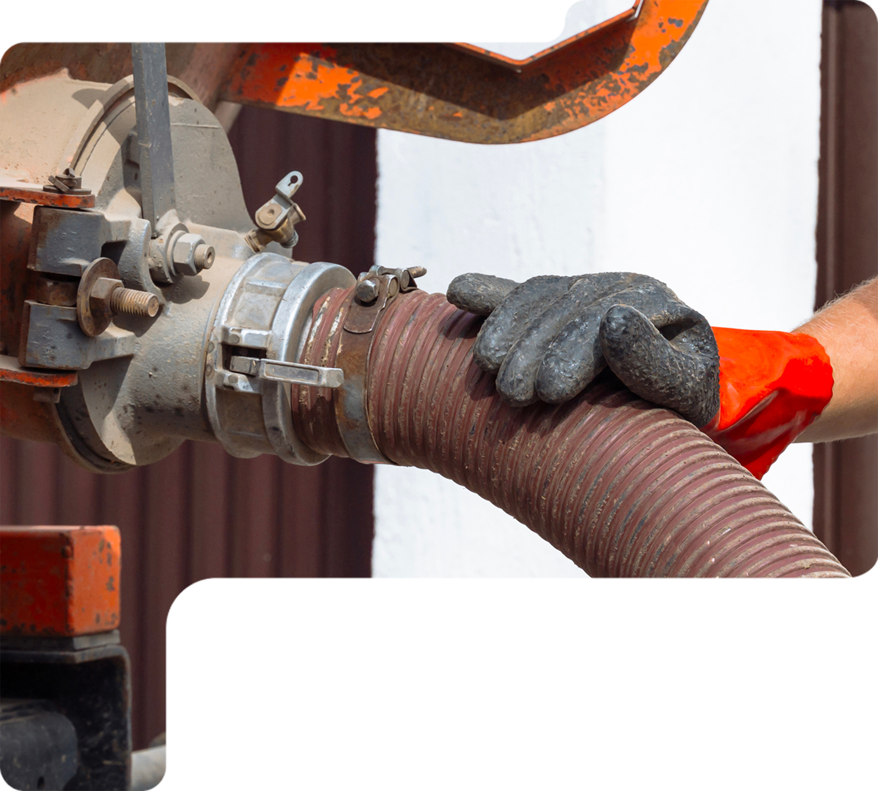 Gloved hand holding a brown hose connected to industrial piping and machinery