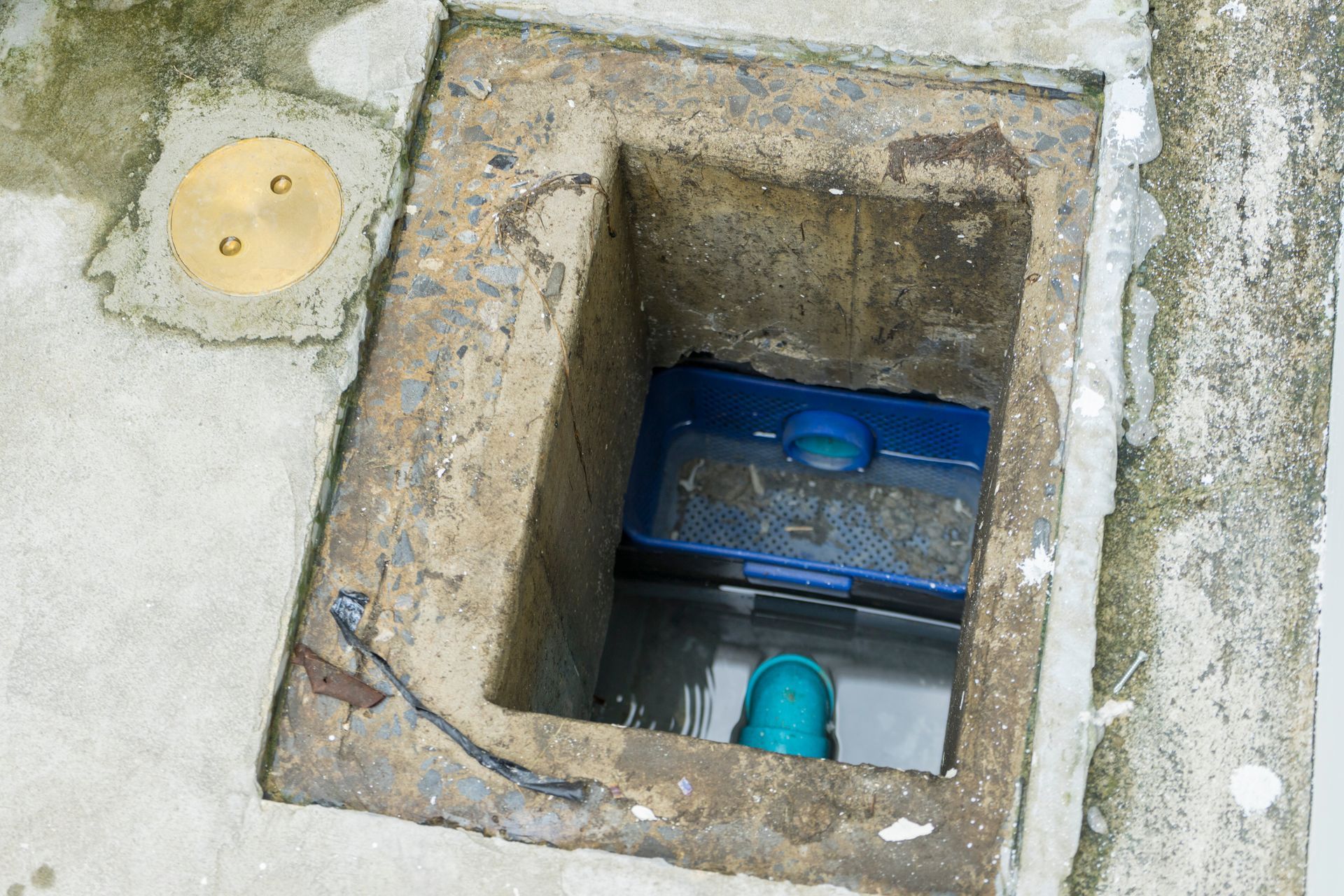 Open concrete utility pit with exposed blue pipe fitting and small yellow cap on pavement.