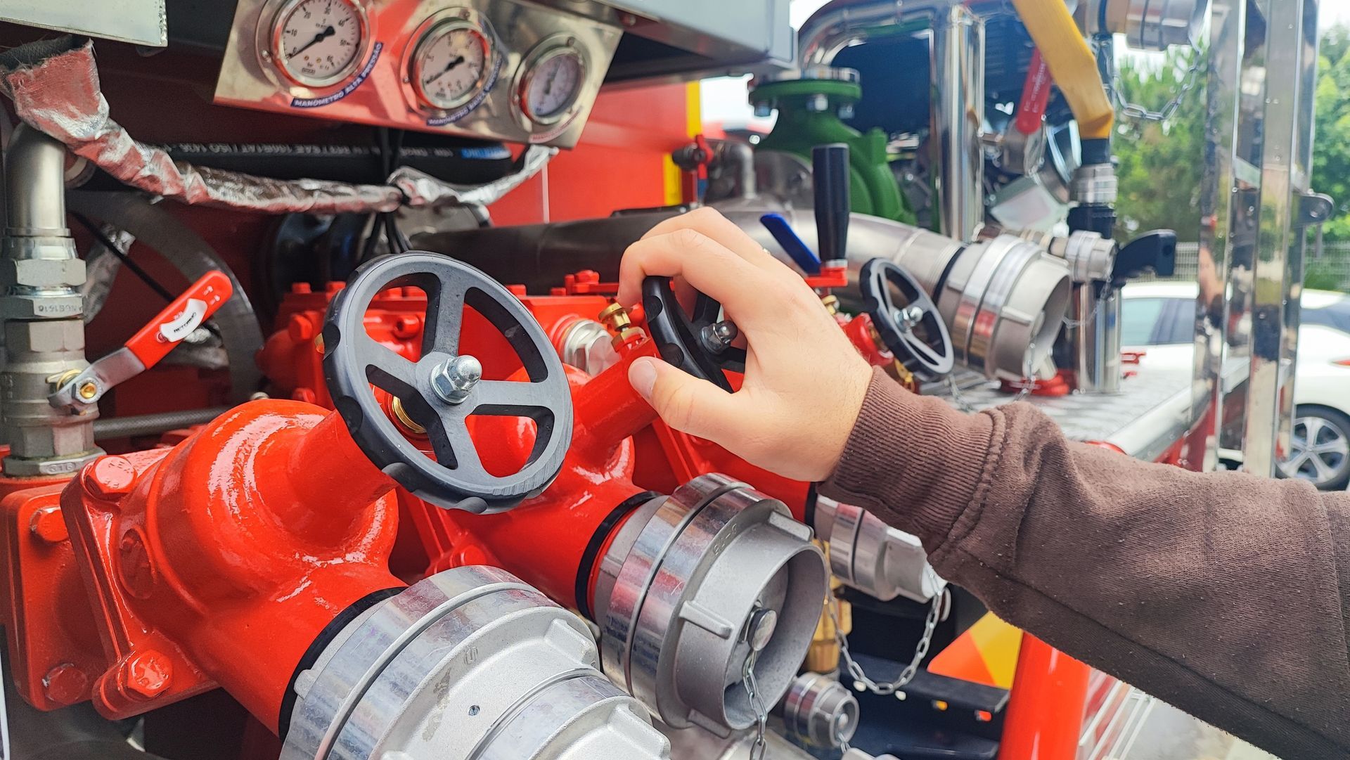 Hand turning a red valve on industrial machinery with gauges and metal pipes nearby