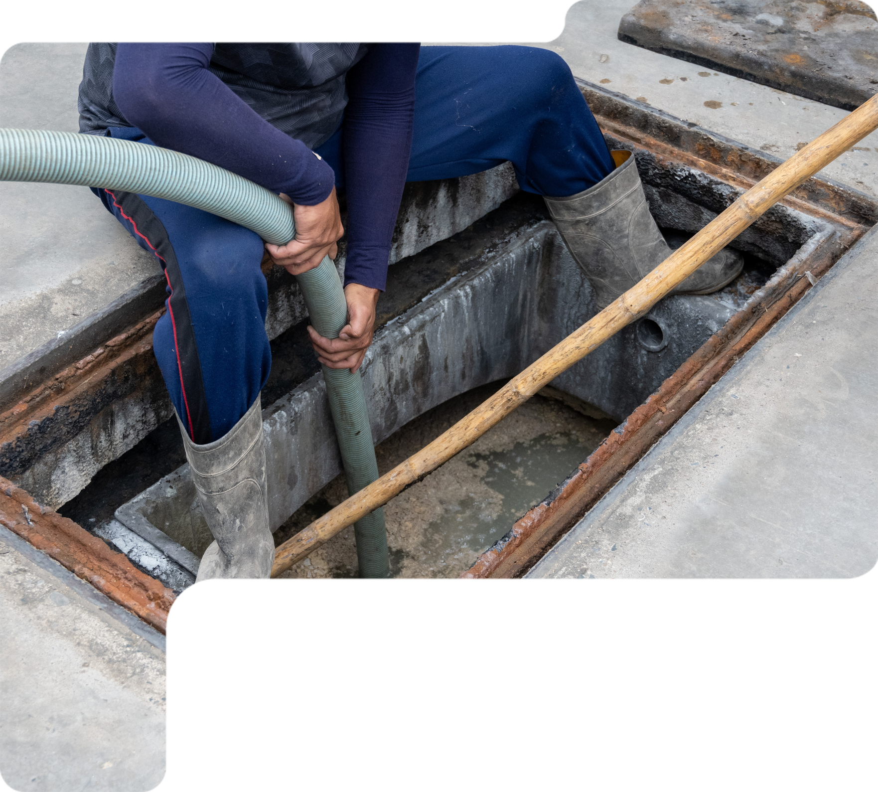Worker cleaning a rectangular concrete pit with a hose and brush