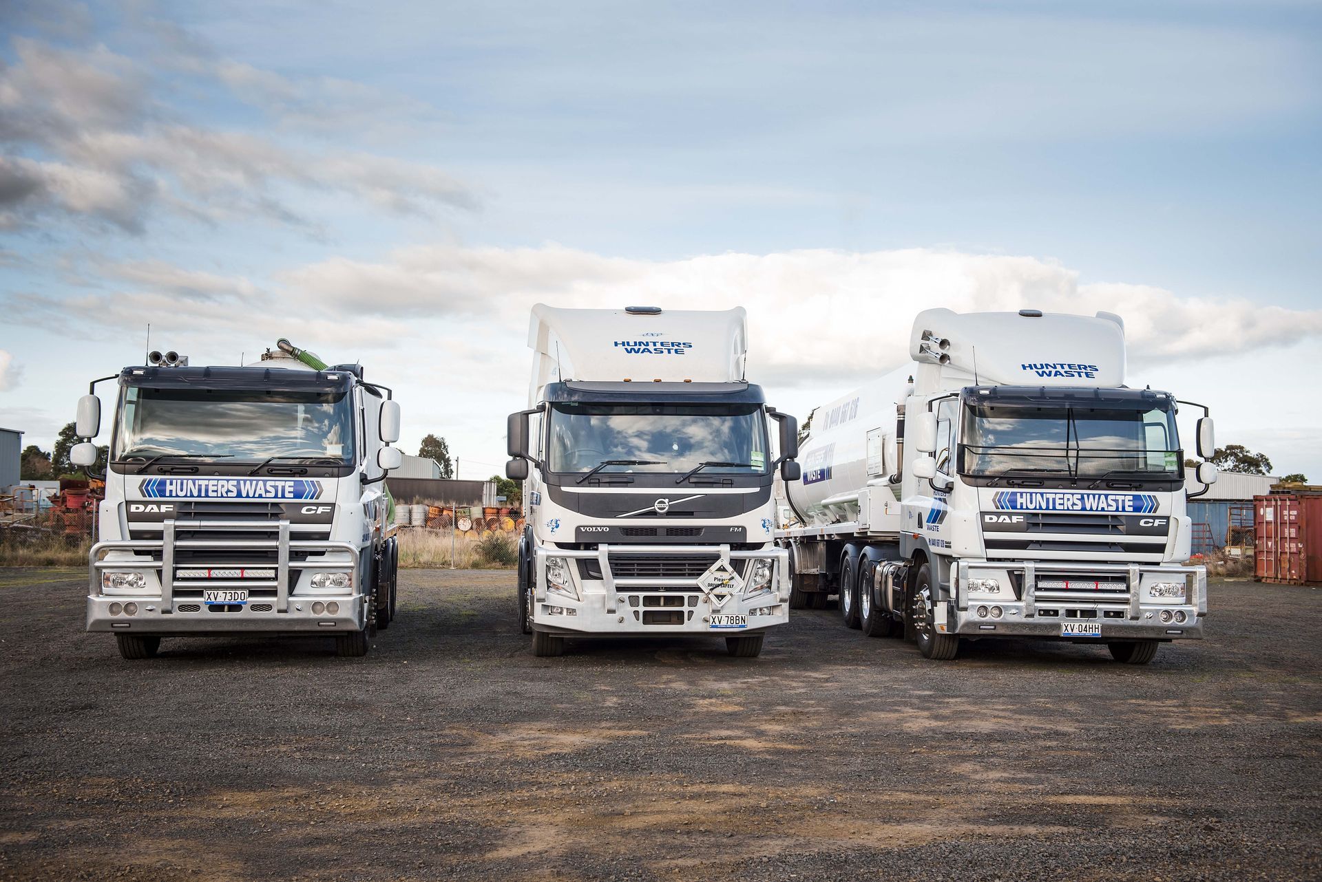 Three white Volvo semi trucks parked side by side on a gravel lot under a cloudy sky