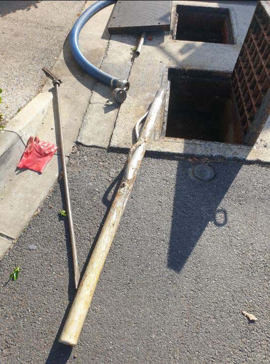 Broken rooftop vent pipe and debris on a gravel roof next to a brick chimney.
