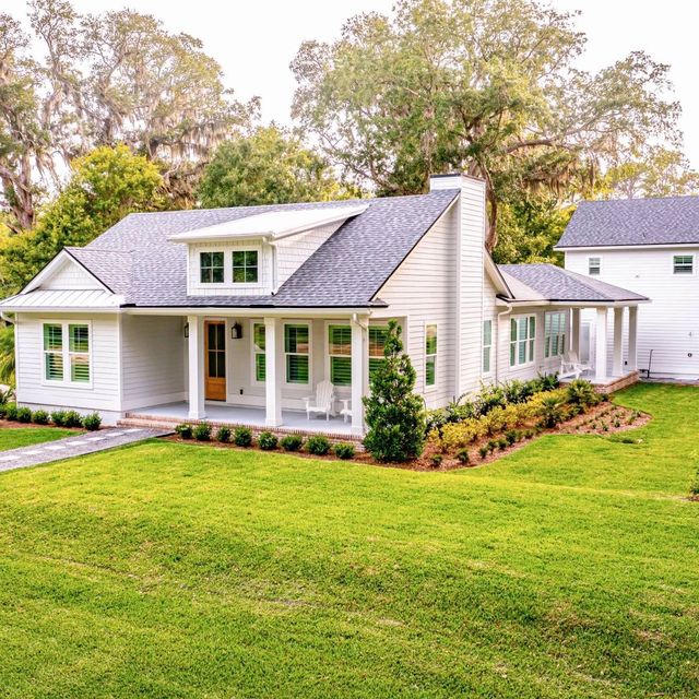 White farmhouse with green lawn and landscaping.