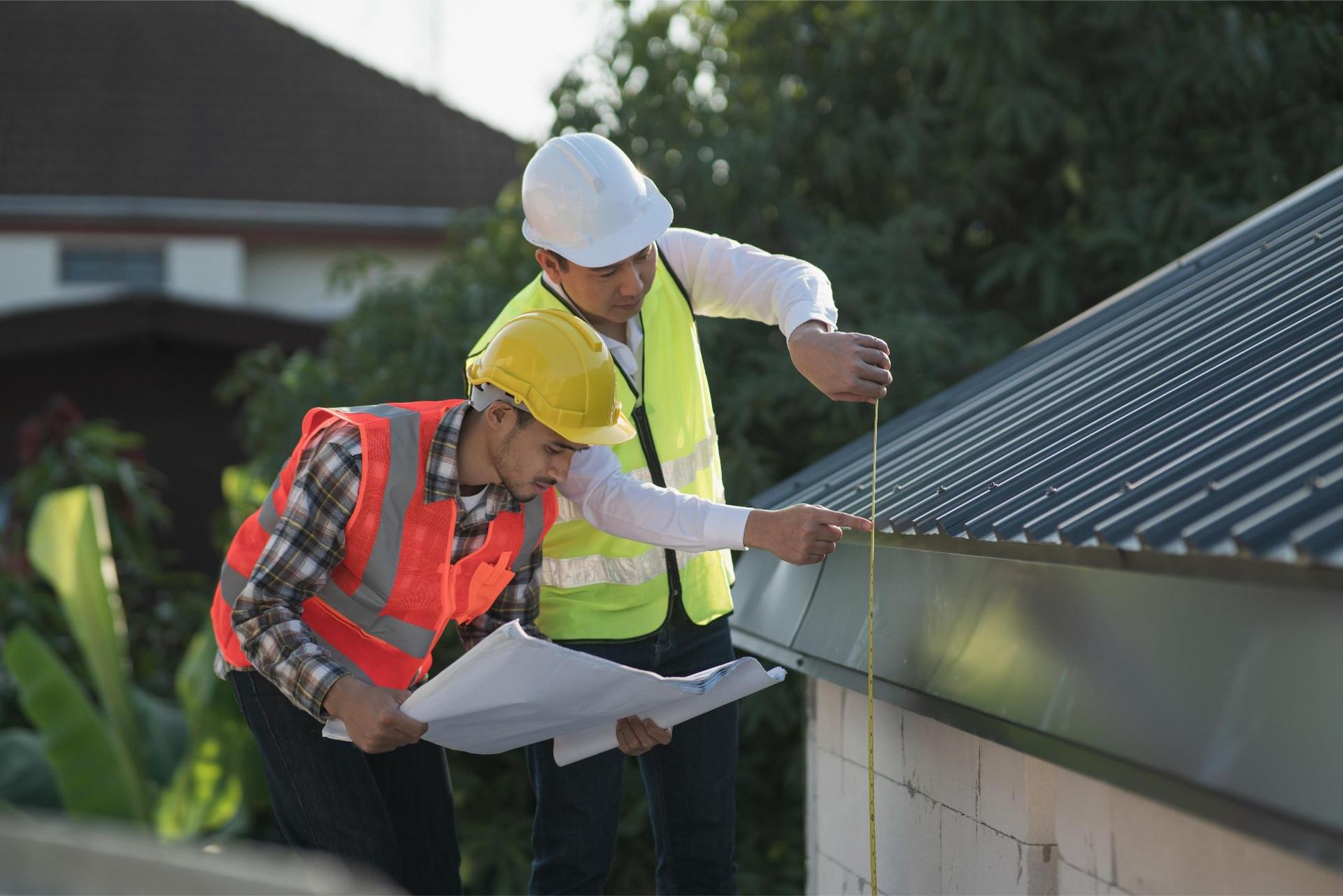 Two workers in hard hats measuring a metal roof on a building site