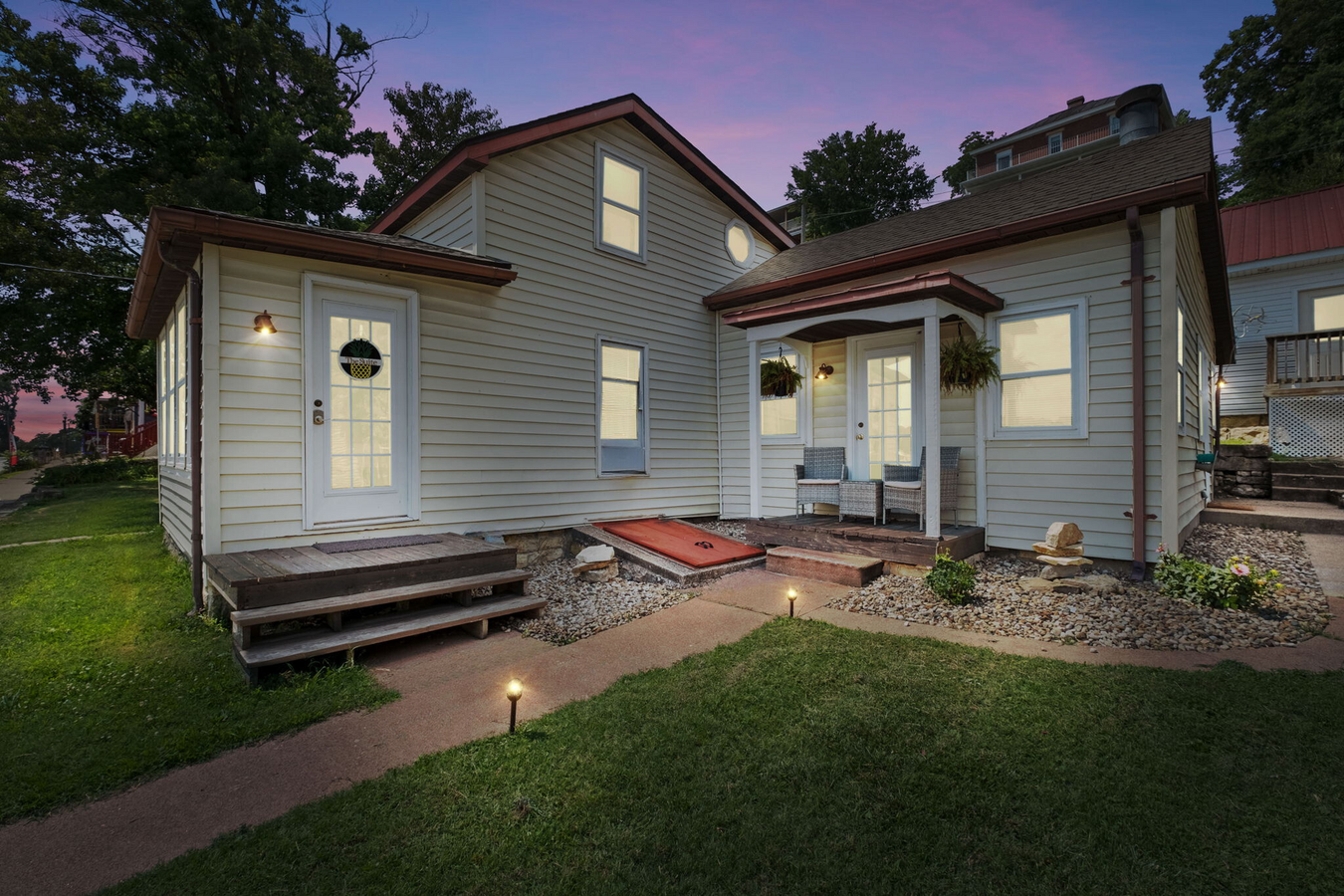 A white house with a porch and stairs is lit up at night.