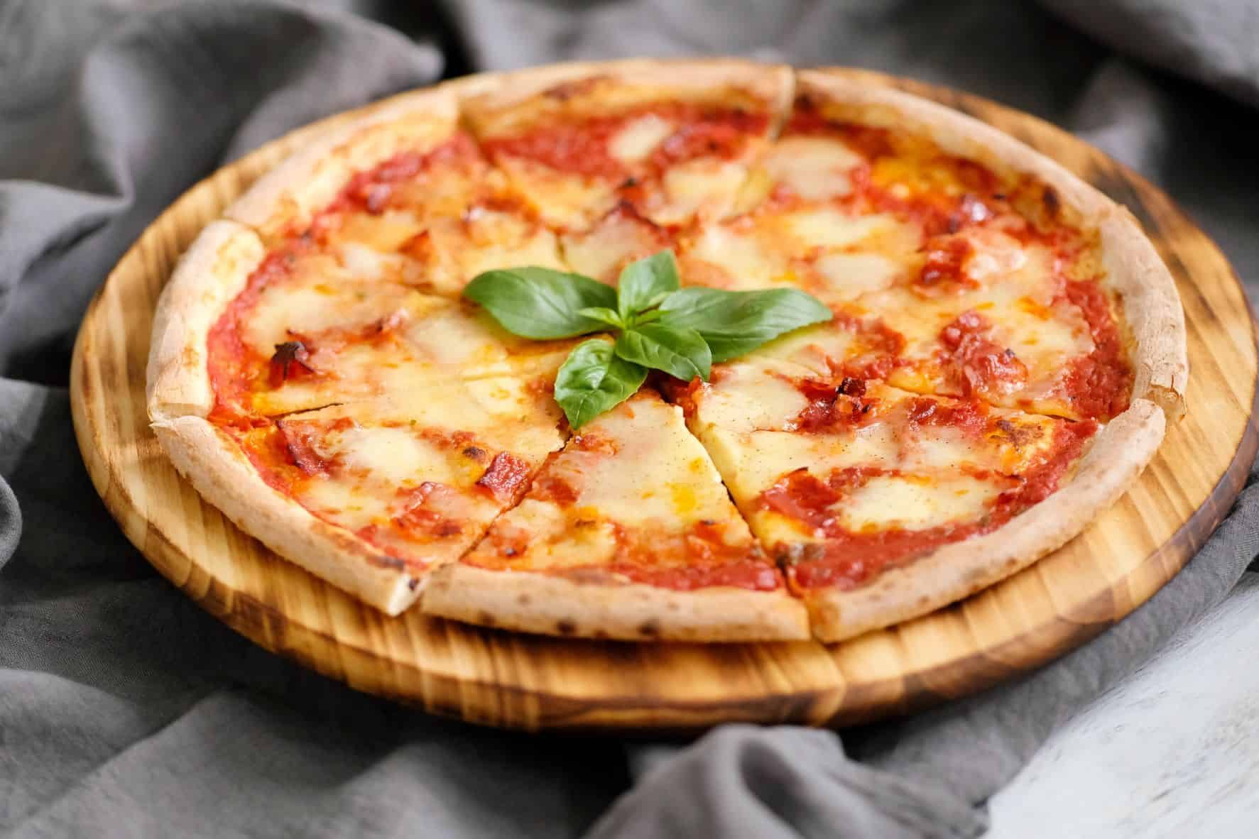 A pizza with tomato sauce and cheese is on a wooden cutting board.