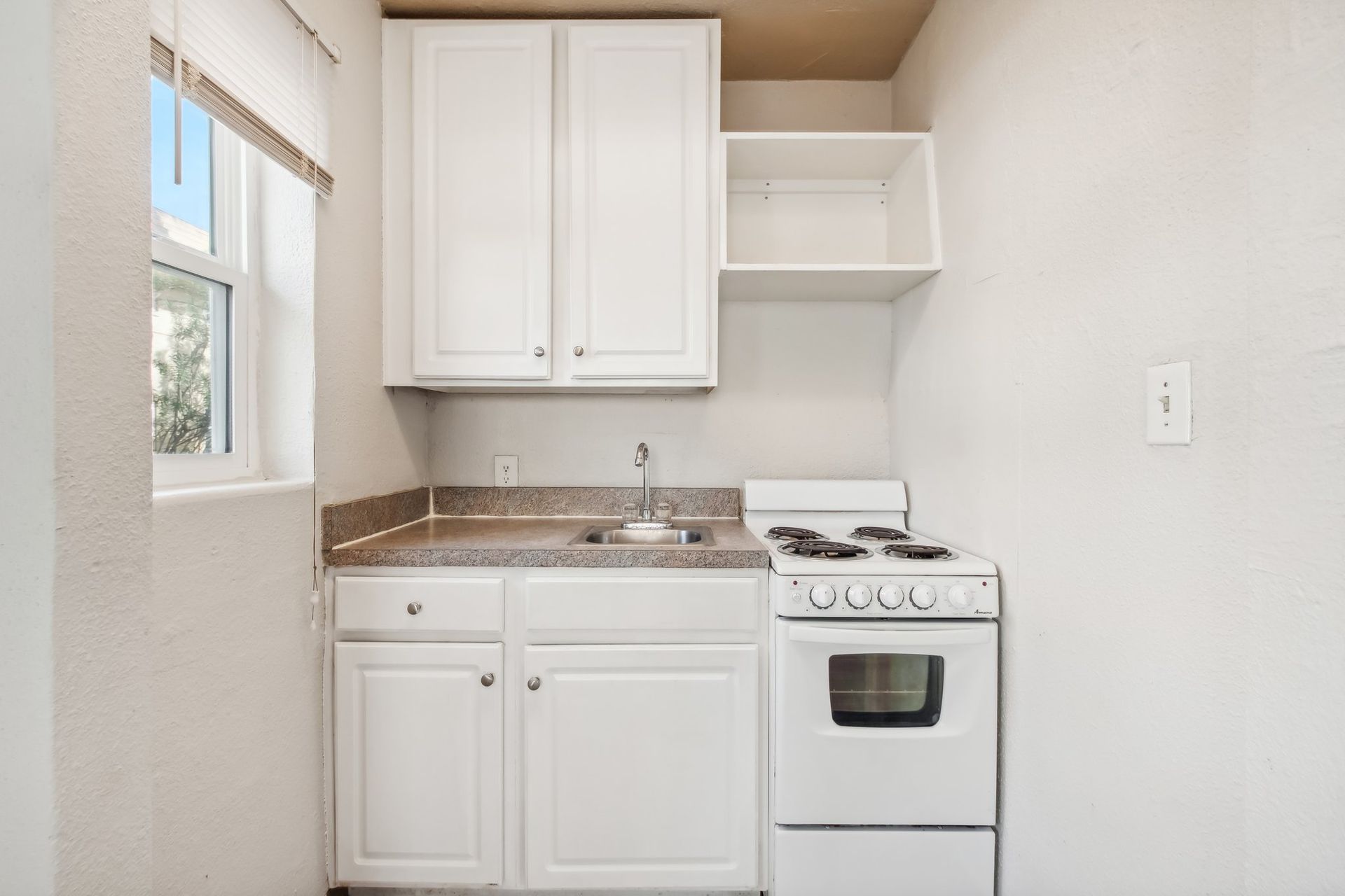 Small white kitchen with cabinets, sink, stove, and a window.