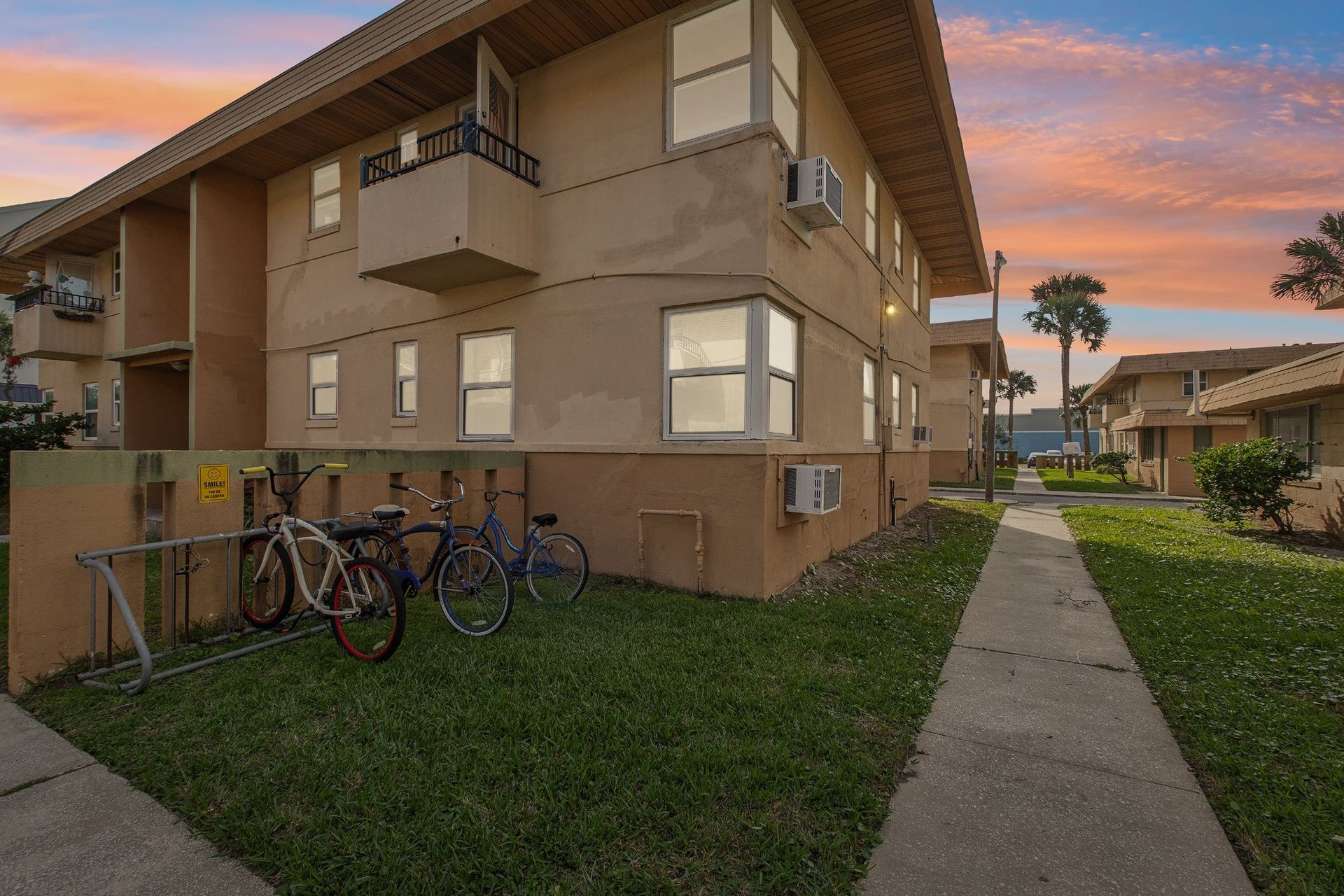 Apartment complex with bikes parked in front, pathway to the right, dusk sky.