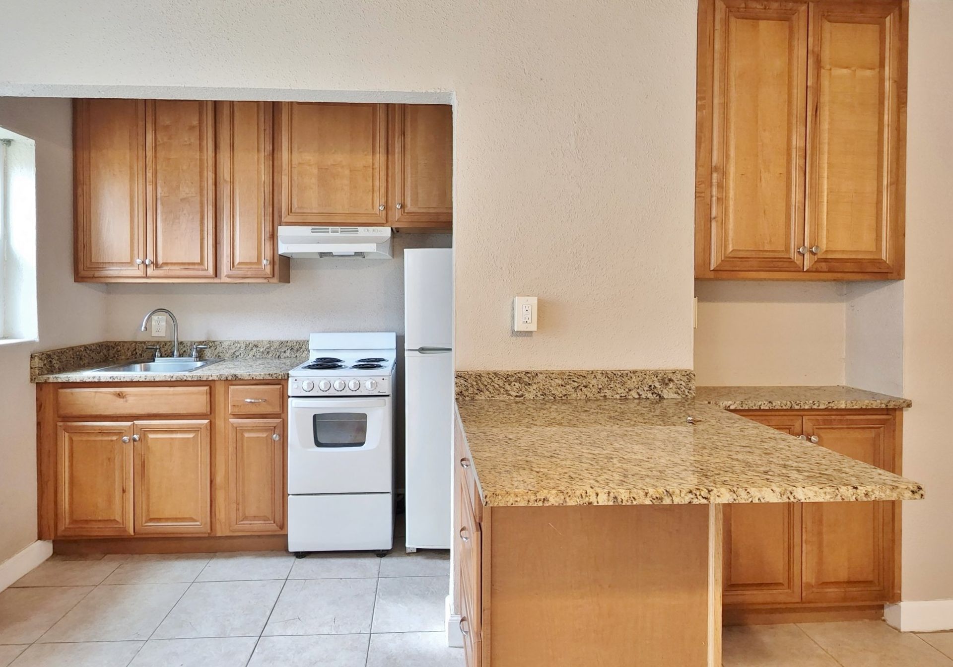 Kitchen with light wood cabinets, granite countertops, white appliances, and a window.