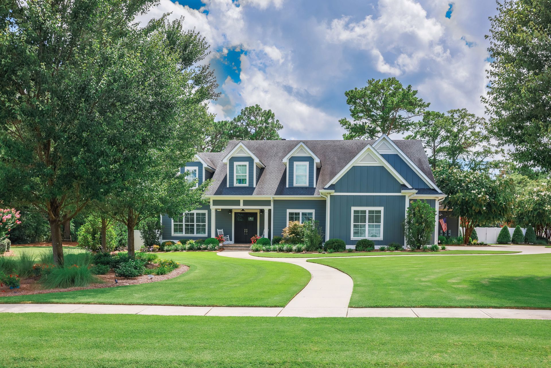 A large blue and white house with a lush green lawn and trees in front of it.