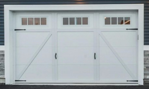 Close-up of a white steel carriage house garage door with a diagonal Z-brace pattern and black decorative hardware